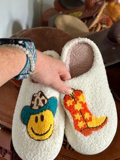 Here’s some fun slippers for the Cowgirls and Cowgirls at heart! These comfy slippers feature a Smiley Face Cowboy and Cowboy Boots. They're incredibly comfy, extra cozy, and feature a rubber bottom ideal for indoor and outdoor wear.Very limited quantity - don't miss out on these fun slippers! Sizing Information:This item is based on women's sizing, and men should size up for the best fit. Size Chart: 6/7: Length 9" 7/8: Length 9 3/4" 8/9: Length 10" 9/10: Length 10 1/2" 11/12: Length 10 3/4" Be Cute Round Toe Slippers For Leisure, Casual Indoor Slippers With Soft Sole, Cute Soft Slippers For Loungewear, Cute Multicolor Slippers With Round Toe, Cute Round Toe Slippers For Loungewear, Playful Winter Slip-on Slippers, White Comfortable Slippers With Soft Sole, Fun White Slip-on Slippers, Comfortable White Slippers With Soft Sole