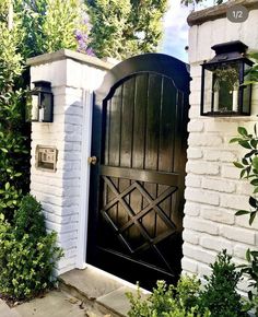 an open black door to a white brick house surrounded by greenery and bushes on a sunny day