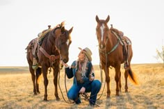 a woman sitting on the ground next to two brown horses in a dry grass field