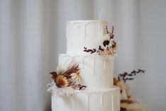 a three tiered white wedding cake with dried flowers