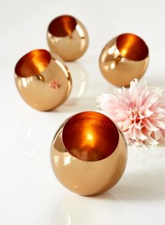 three copper colored vases sitting on top of a white table next to a pink flower