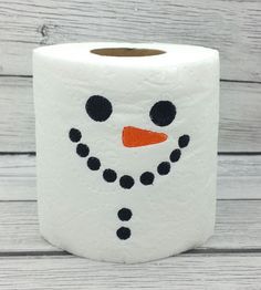 a toilet paper roll with a snowman face painted on the front and sides, sitting on a wooden surface