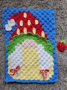 a crocheted square with a red strawberry on the side and a blue background