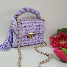 a purple crocheted purse sitting on top of a table next to a pink flower