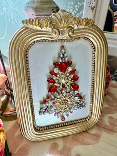 an ornate gold frame with a red and white christmas tree brooch in the center