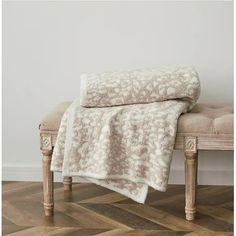 a bench with a blanket on it in front of a white wall and wooden floor