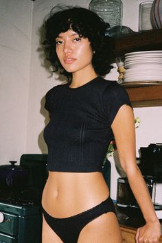 a woman in a black top and panties standing next to a counter with dishes on it