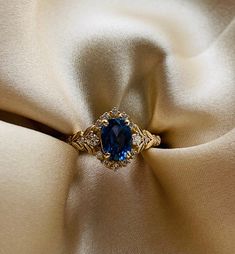 a blue stone ring sitting on top of a white satin material with gold trim around it