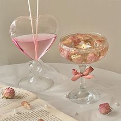 two glasses filled with pink liquid sitting on top of a table next to an open book