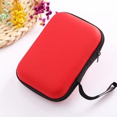 a red case sitting on top of a white table next to a basket with flowers