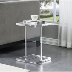 a glass end table with a bowl on it in front of a couch and window