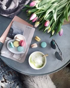 a table topped with plates and cups filled with macaroons next to a bouquet of tulips