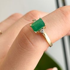 a close up of a person's hand holding a ring with a green stone on it