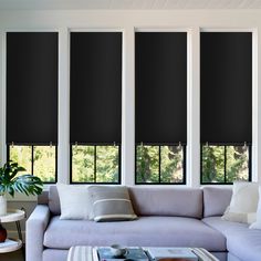 a living room with three windows covered in black shades and white pillows on the couch