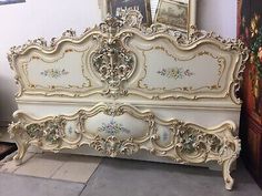 an ornate white bed frame with gold trimmings and flowers on the headboard