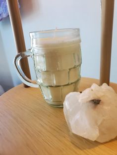 a candle sitting on top of a wooden table next to a glass cup filled with liquid