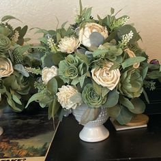 two white vases filled with flowers on top of a black table next to a book