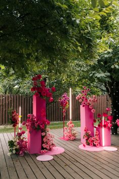 three pink vases with flowers and candles are on the ground in front of some trees