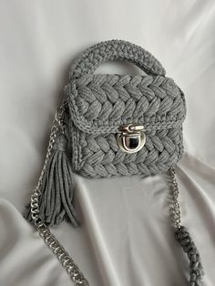 a gray handbag on a white bed with a chain around the strap and clasp