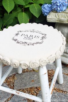 an old stool with the word paris painted on it and some flowers in the background