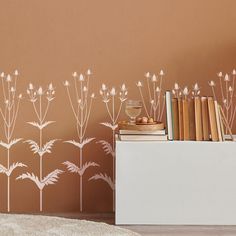 a book shelf with books on top of it next to a wall with flowers painted on it