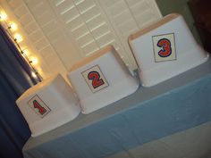 three white stools sitting on top of a blue tablecloth covered table with lights in the background