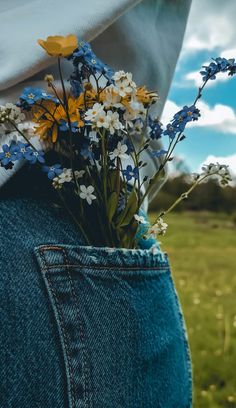 a person with their back to the camera holding flowers in his jeans pocket while standing in a field