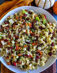 a white bowl filled with pasta salad next to two pumpkins and an orange towel