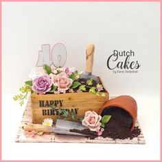 a birthday cake with flowers in a wooden box and a shovel on the table next to it