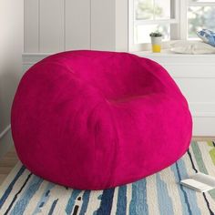 a bright pink bean bag chair sitting on top of a rug next to a window