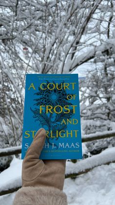 a person holding up a book in front of snow covered trees and branches with the title a court of frost and starlight written on it