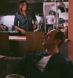 a man sitting on top of a couch in a kitchen next to a woman standing behind him