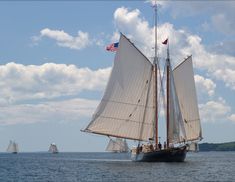 two sailboats sailing in the ocean with an american flag on their sails and another boat behind them