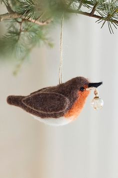 a bird ornament hanging from a tree branch with a bead in it's beak