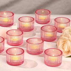 pink glass tealight candles are arranged on a white surface with a rose in the background