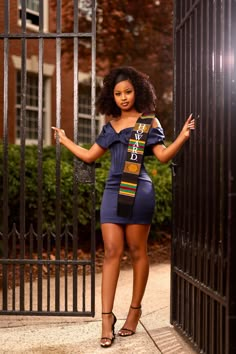 a woman standing in front of an iron gate wearing a blue dress and black heels