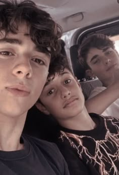 three young men sitting in the back seat of a car, one is looking at the camera