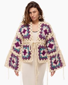 a woman is wearing a crocheted jacket with tassels on the sleeves