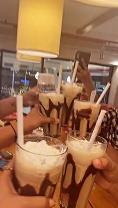 four people holding up glasses filled with liquid and straws in front of the camera