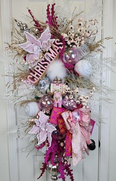 a pink and white christmas wreath hanging on the front door