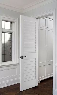 an empty room with white walls and wooden flooring, two open doors leading to another room