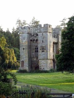 an old castle sitting in the middle of a lush green field with trees around it