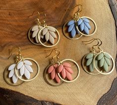 four pairs of earrings with leaves on them sitting on top of a piece of wood