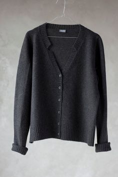 a gray sweater hanging on a white hanger with a black button up shirt underneath it