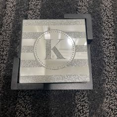 the letter k is engraved on an acrylic box that sits on carpeted area