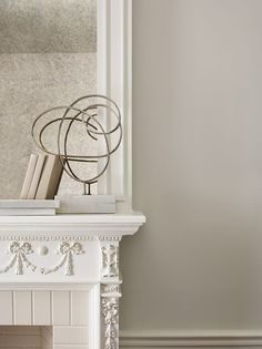 a white fireplace mantel with books on top and a metal sculpture in the corner