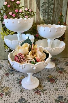 three white dishes with flowers in them sitting on a floral tablecloth next to each other