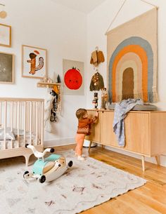 a small child playing with toys in a white room next to a dresser and crib