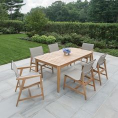 a wooden table with chairs around it in the middle of a patio area surrounded by greenery