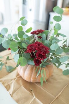 a vase filled with red flowers sitting on top of a brown paper covered tablecloth